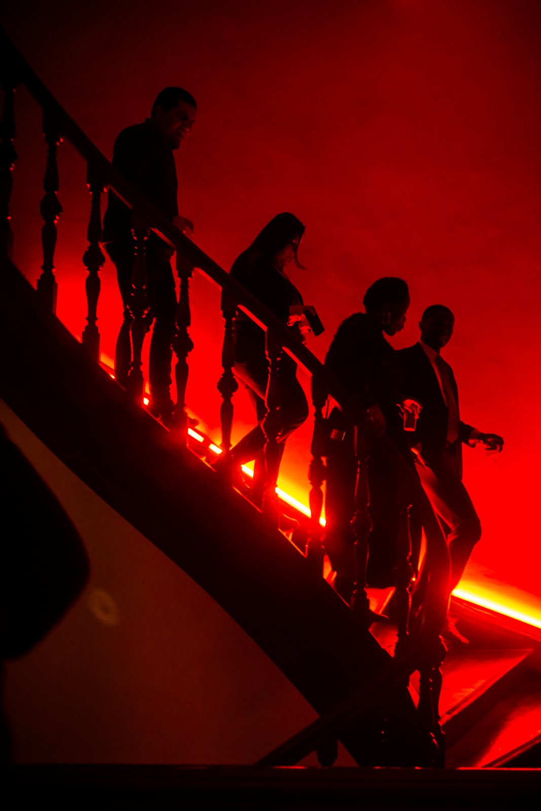 Guests in silhouette walking down a red-lit staircase, away from the viewer