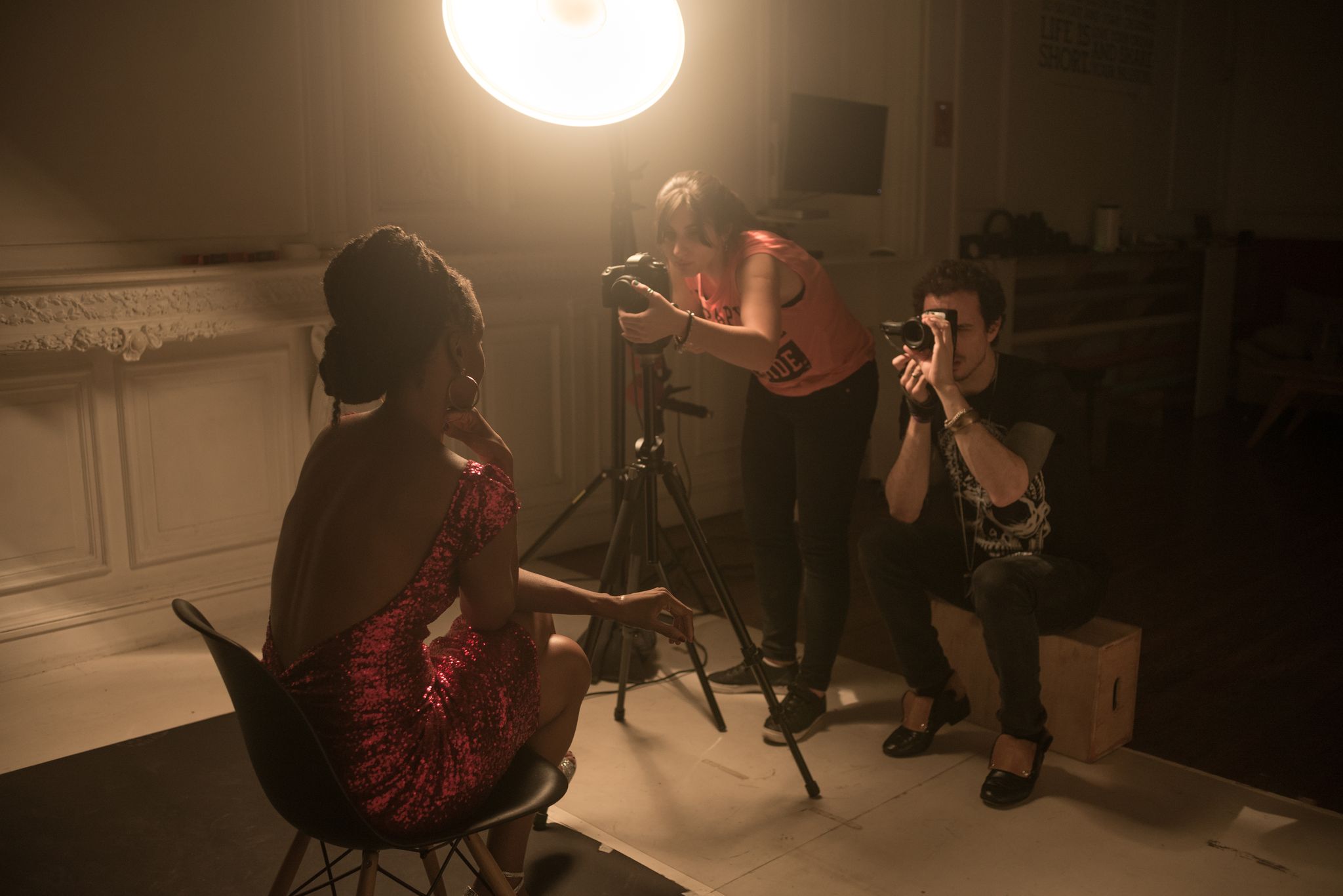 Behind the scenes at a photo shoot: a woman in a red sequined dress poses while two photographers work under a studio light