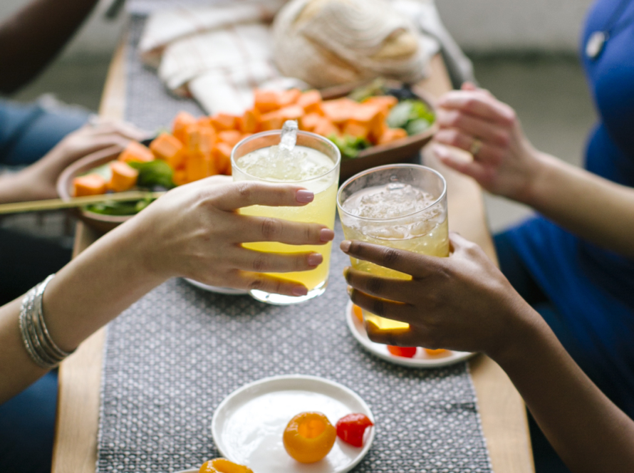 black and white hands holding cold beverges and making a cheers, over appetizers at a table