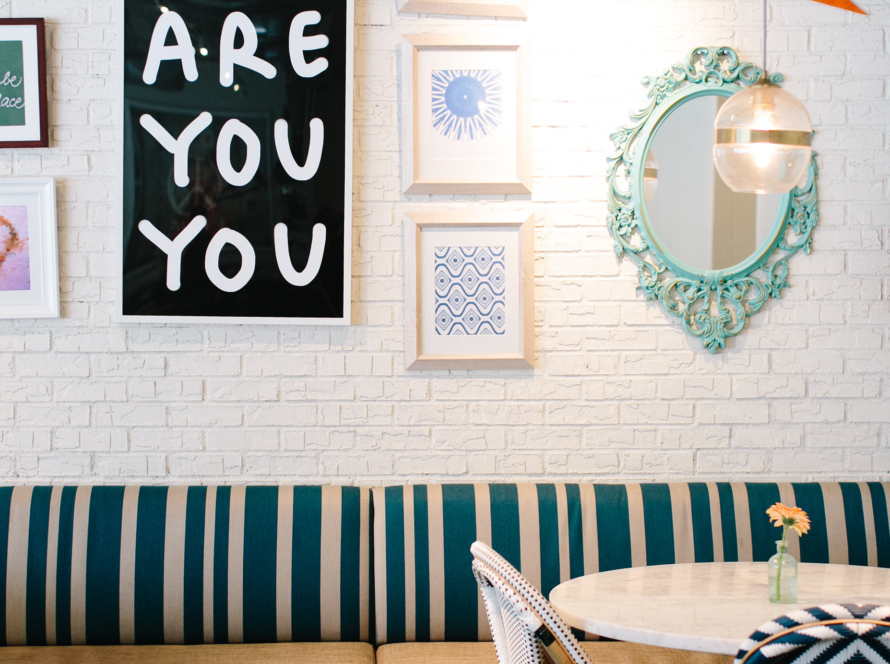 We can see a neat living room, decorated with an orange pennant, a very nice mirror with a tie in its frame and other paintings on a white wall. The furniture is a mixture of rustic and modern