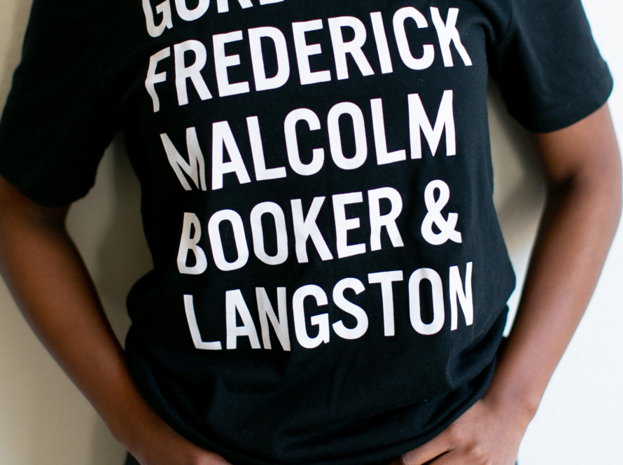 In the image we can see a black woman, with a black shirt and white letters.