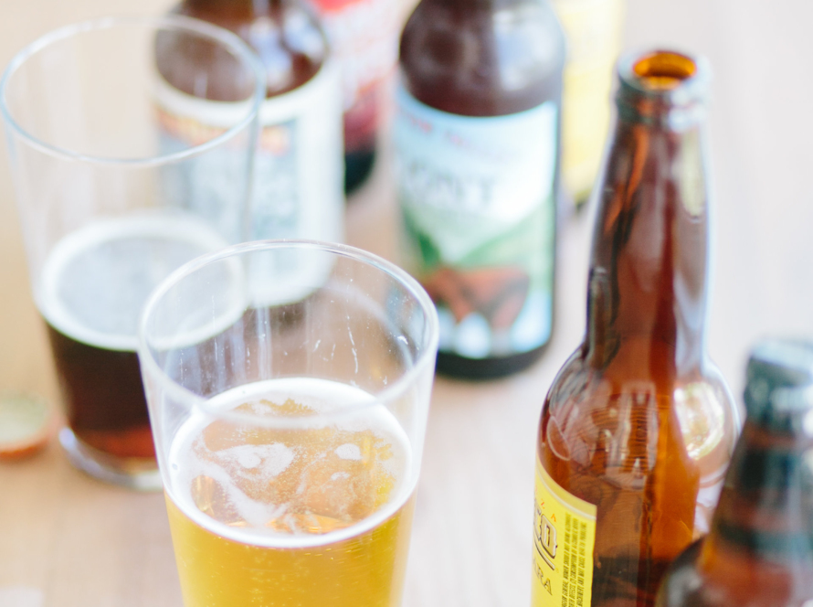 In the image, we can see several bottles of beer and two glasses on a table. one, with lager and the other, with stout.