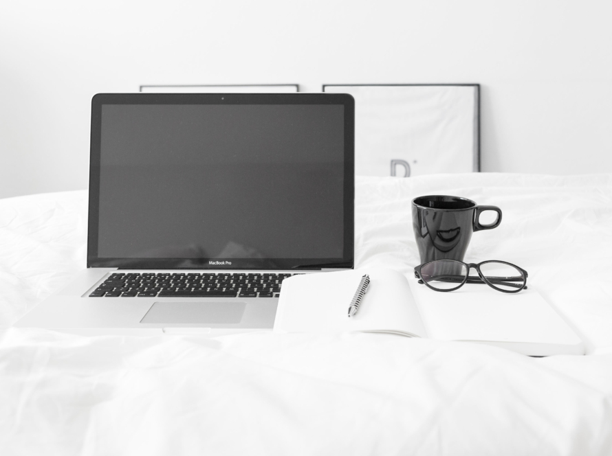 In the image we can see in a white room, a round table of the same color, on which we find a laptop, a black pen and cup, plus a notebook.