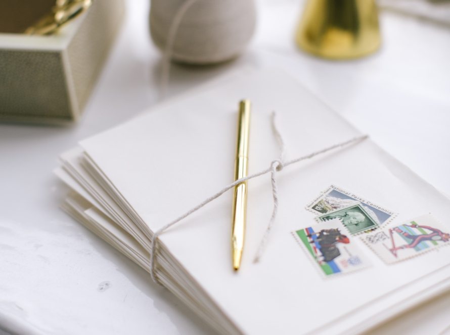 In the image we can see correspondence, a gold pen, a roll of thread on a white table.