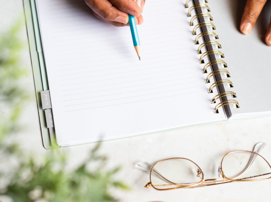 In the image we can see an agenda, and the hands of a black woman, taking notes.