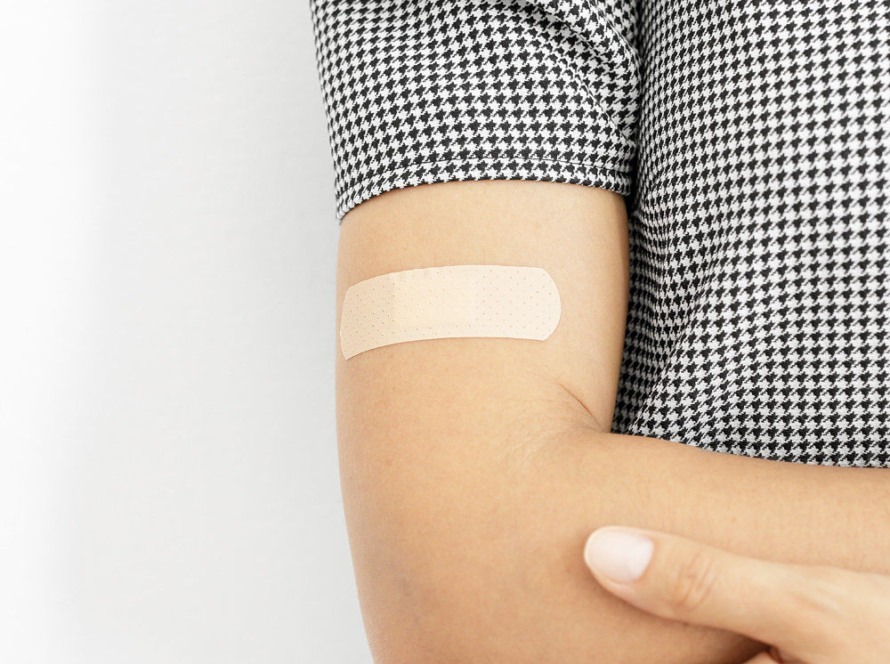 In the image we can see the right half of a woman's torso, wearing a short-sleeved blouse and a small dressing on her arm.