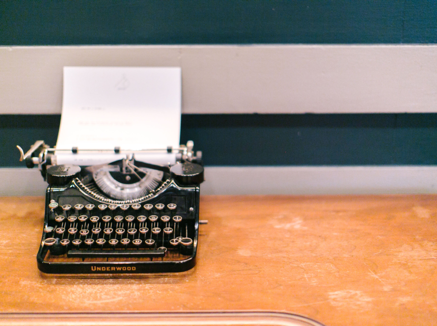 In the image we can see an old typewriter, on the desk of a school classroom