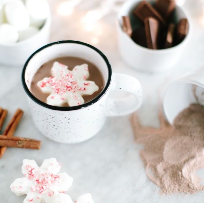 In the image, we can see a cup of coffee on a delicately decorated table, with cinnamon and chocolate bars.