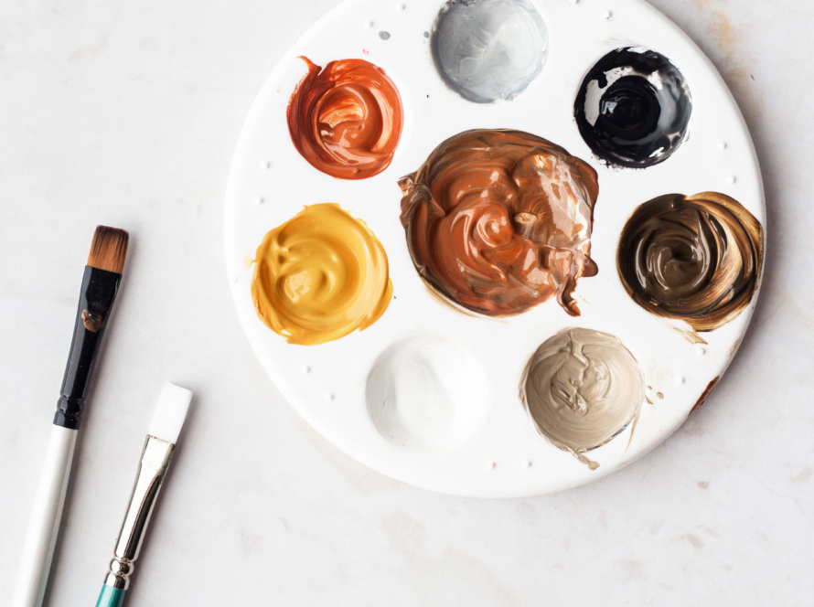 In the image, we can see a circular paint palette with pastel watercolors and two brushes.