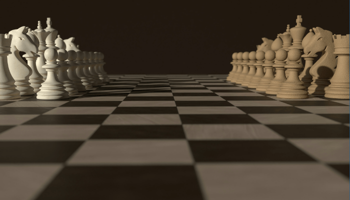 A black and white chess board. On the left side are cream colored pieces. And on the right side, are beige pieces