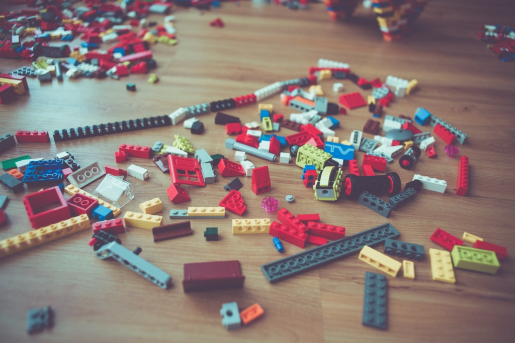 A wood floor has a bunch of colored legos of all shapes and sizes strewn all over the floor. 