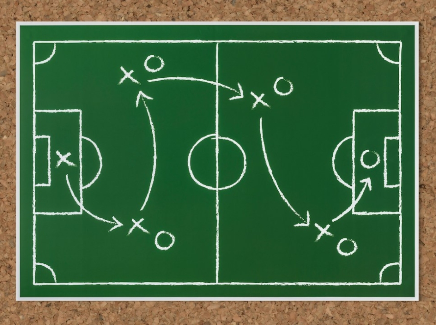 a corkboard that has an image of a green soccer (football) field on it, and there are plays on it -- like a playbook.