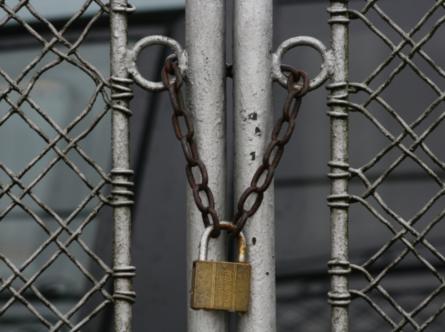 Close-up of a metal chain and padlock securing a closed wire fence gate, symbolizing barriers that prevent customers from moving forward.