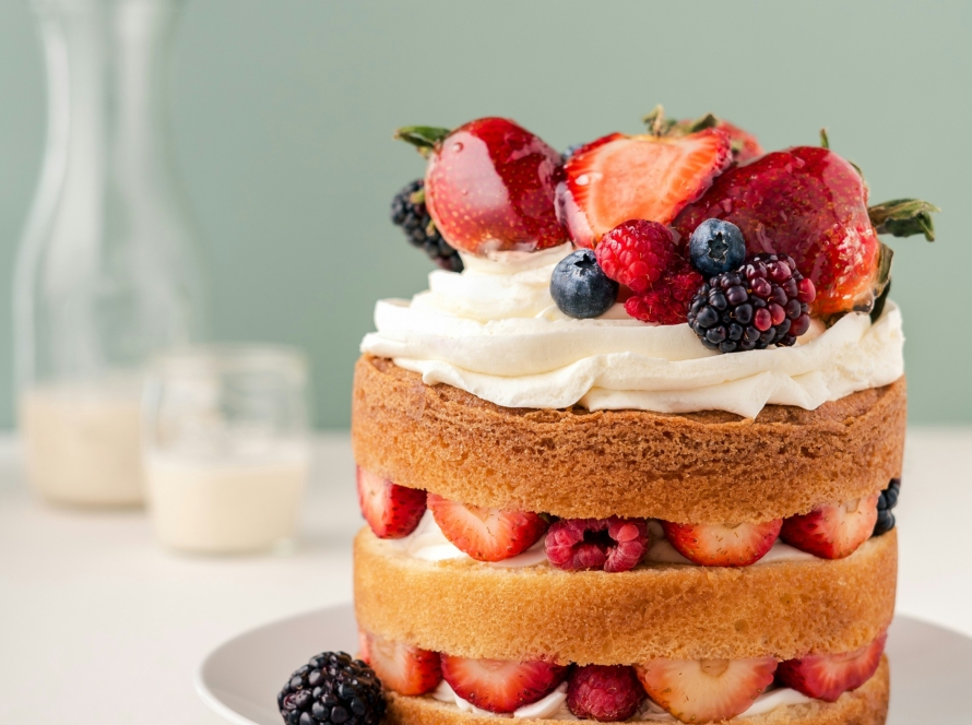 Layered strawberry and mixed berry cake with whipped cream on a white plate.