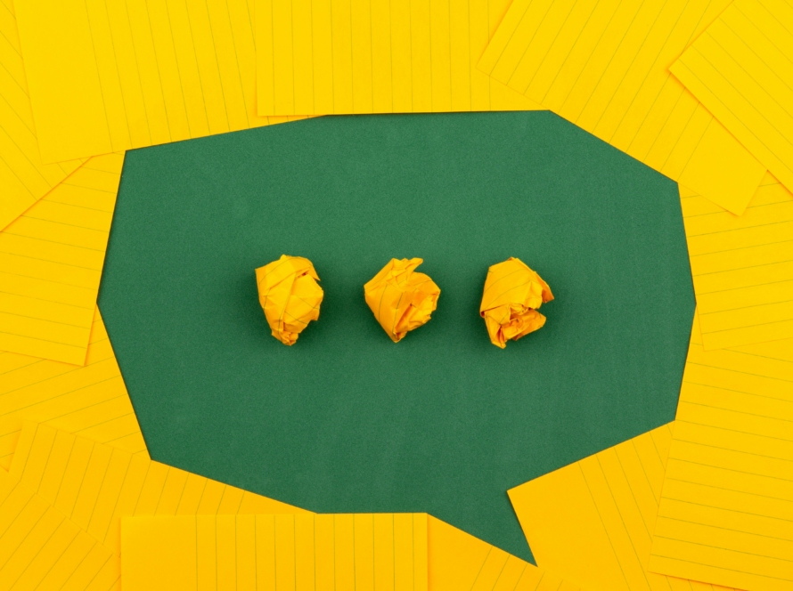 Green speech bubble surrounded by yellow paper, with three crumpled yellow paper balls representing messages or communication.